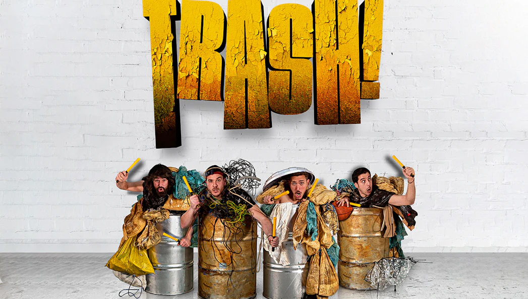 Performers in barrels with props under "Trash!" sign for Yllana & Toom Pak show.
