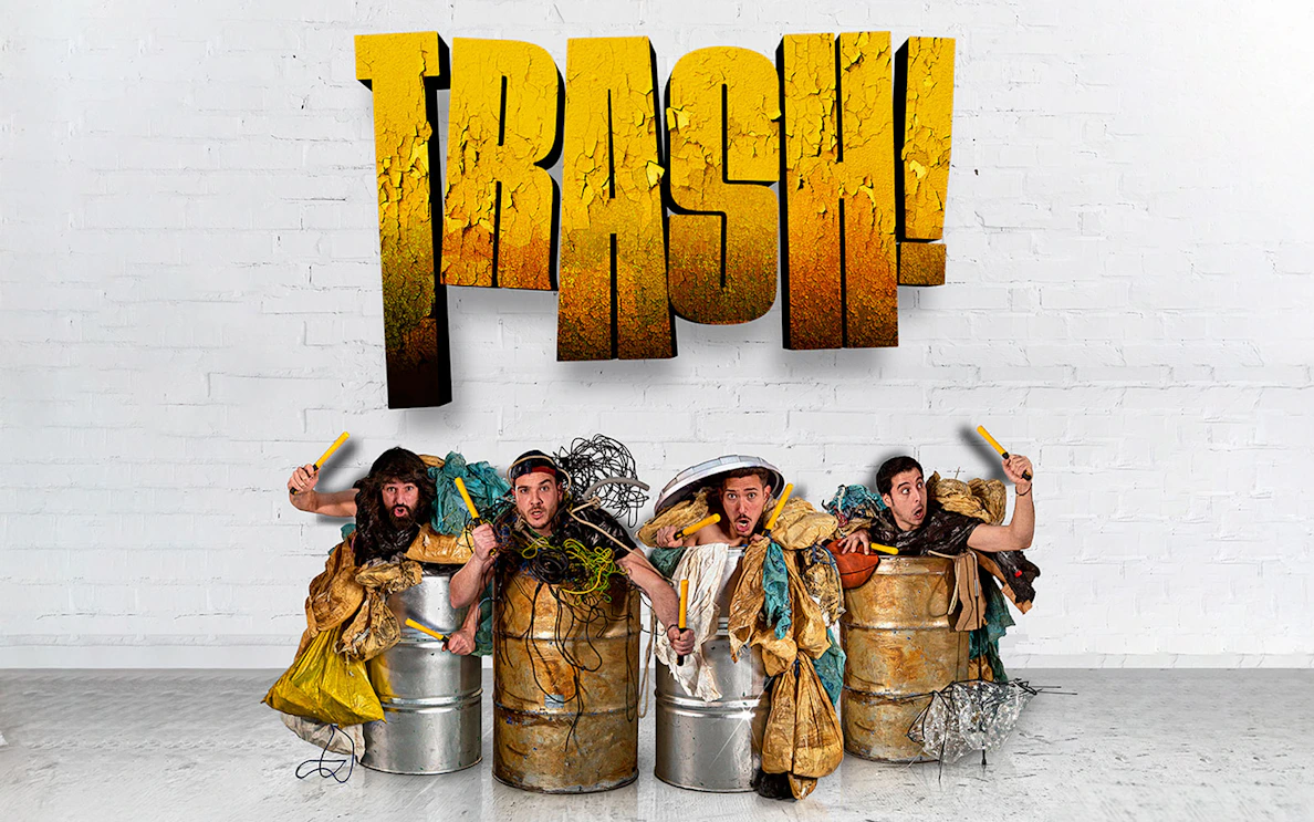 Performers in barrels with props under "Trash!" sign for Yllana & Toom Pak show.