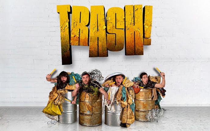 Performers in barrels with props under "Trash!" sign for Yllana & Toom Pak show.
