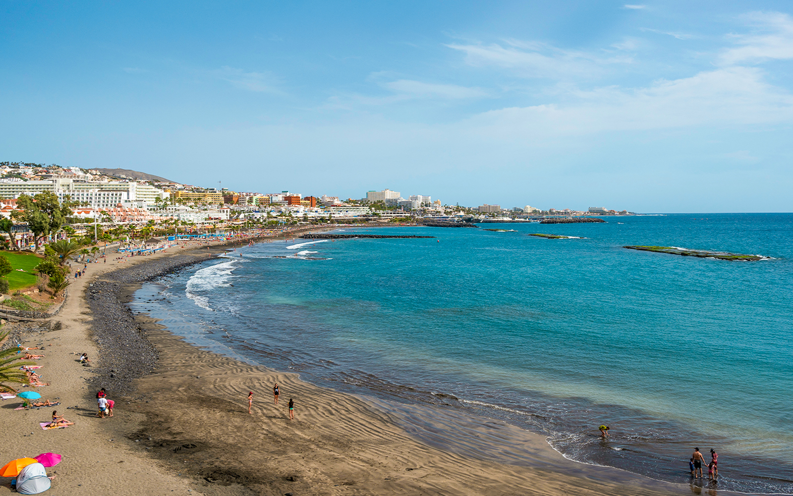 Playa de Fanabe beach with volcanic sand and tourists in Tenerife, Spain.