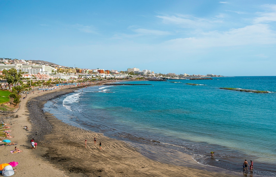 Playa de Fanabe beach with volcanic sand and tourists in Tenerife, Spain.
