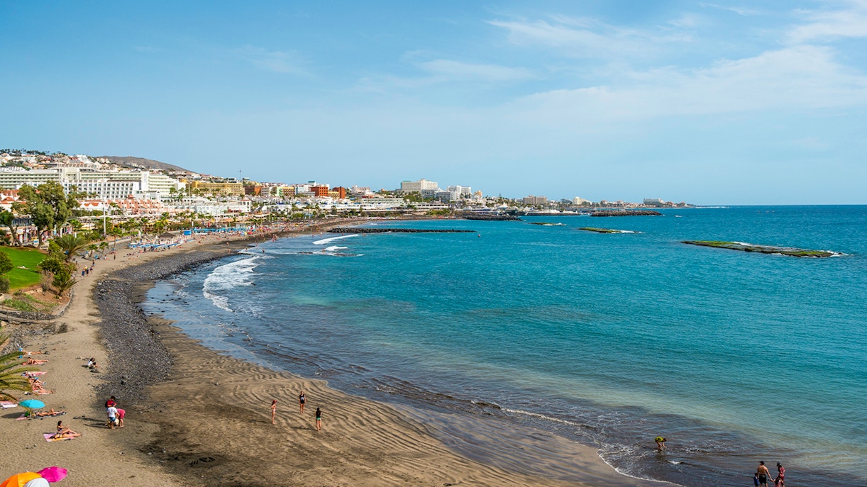 Playa de Fanabe beach with volcanic sand and tourists in Tenerife, Spain.