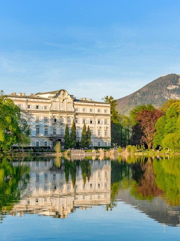 Leopoldskron Palace reflecting in a lake with mountains in Salzburg.