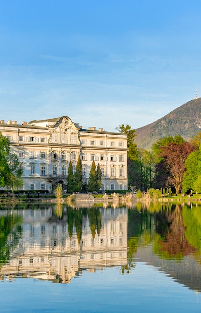 Leopoldskron Palace reflecting in a lake with mountains in Salzburg.