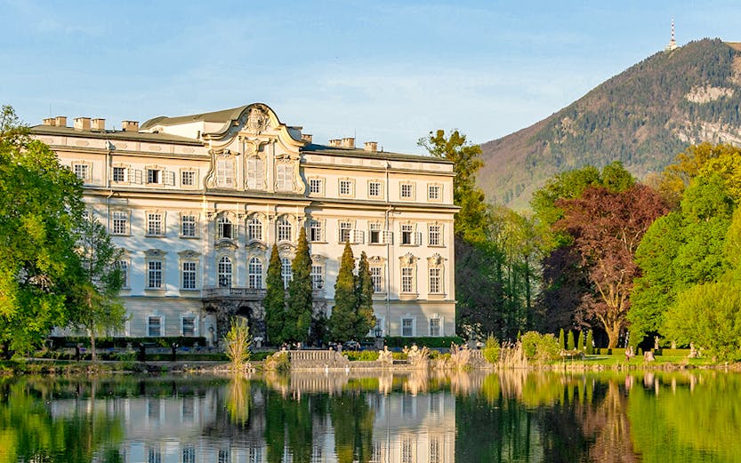 Leopoldskron Palace reflecting in a lake with mountains in Salzburg.