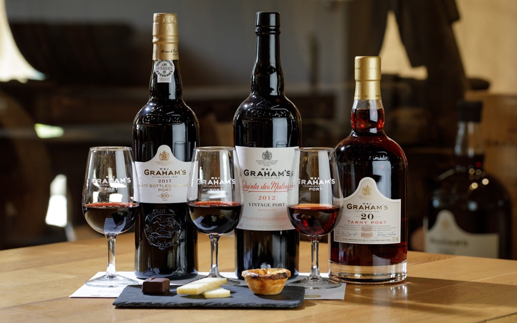 Graham’s Port wine bottles and glasses with cheese and chocolate on a table.