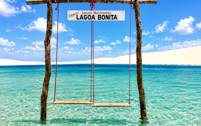 Swings over clear water at Lagoa Bonita, Barreirinhas, with sand dunes in the background.