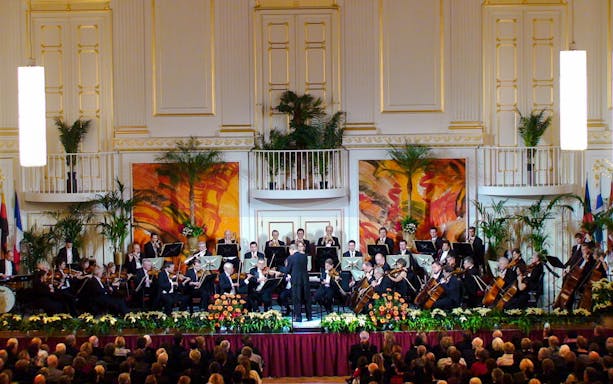 Vienna Hofburg Orchestra performing with musicians playing violins and flutes on stage.