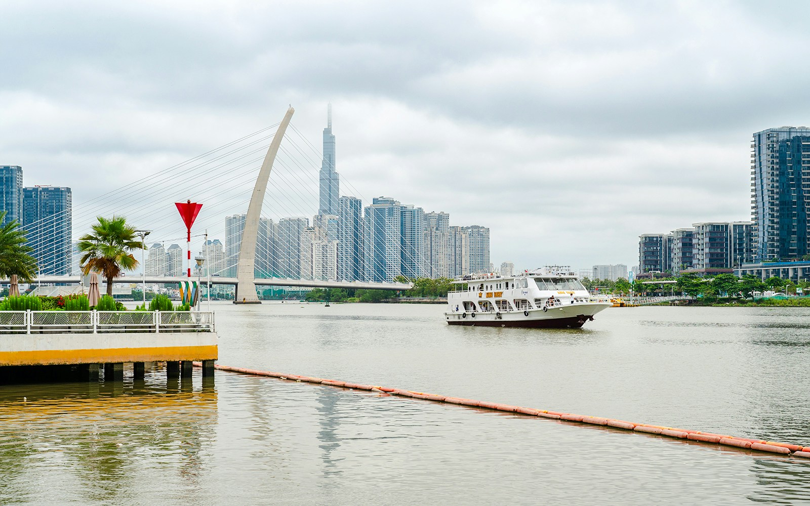 Cruise boat on Saigon River with city skyline and bridge in the background.