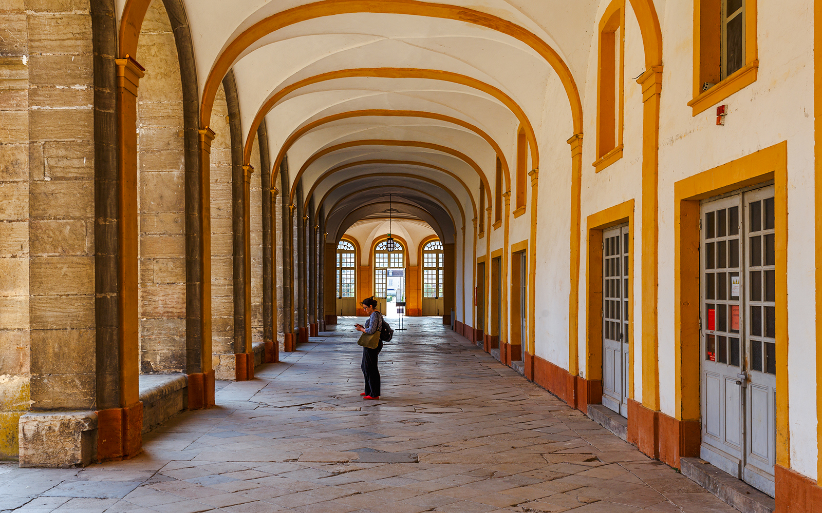 Interior corridor of Abbaye de Cluny, Lyon, France, with a person standing and observing.