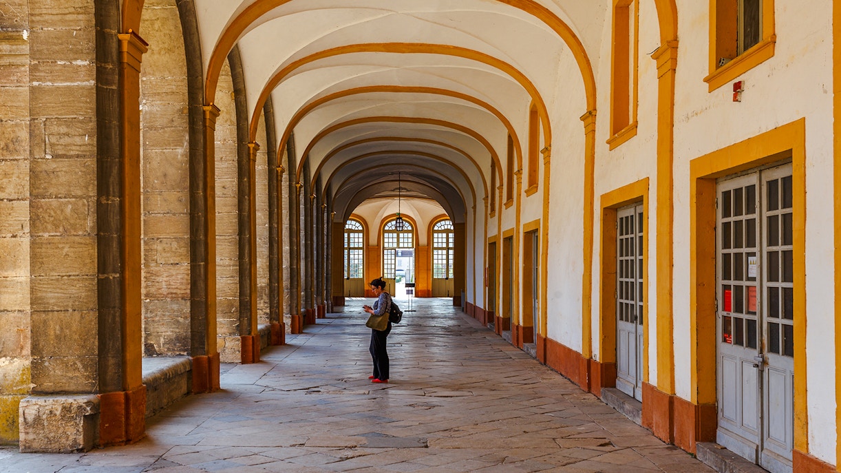 Interior corridor of Abbaye de Cluny, Lyon, France, with a person standing and observing.