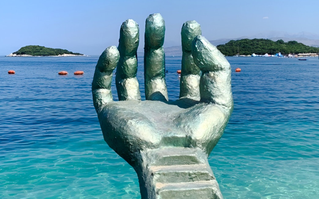 Sculpture of a hand emerging from the sea at Ksamil Beach, Albania.