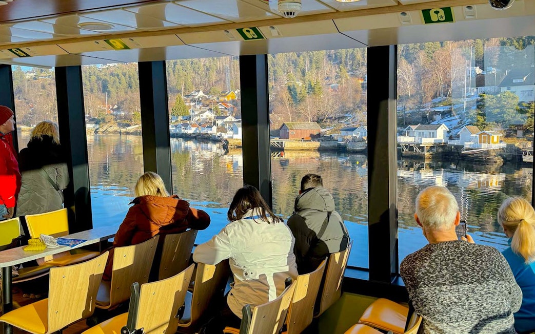 Sightseeing cruise passengers view Oslo fjord landscape through large windows.