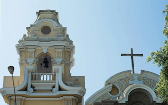 Bell tower and cross of a historic church in Barranco, Lima, on a clear day.