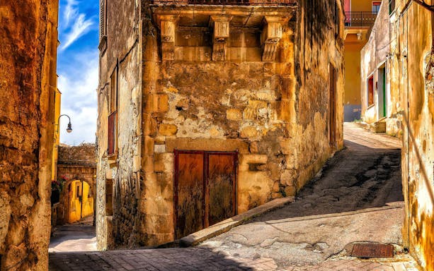 Narrow cobblestone street in Ragusa with historic stone buildings.