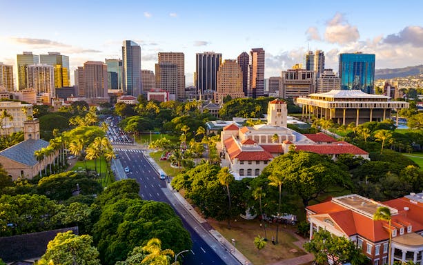 Honolulu Hale with surrounding greenery and Honolulu skyline in the background.