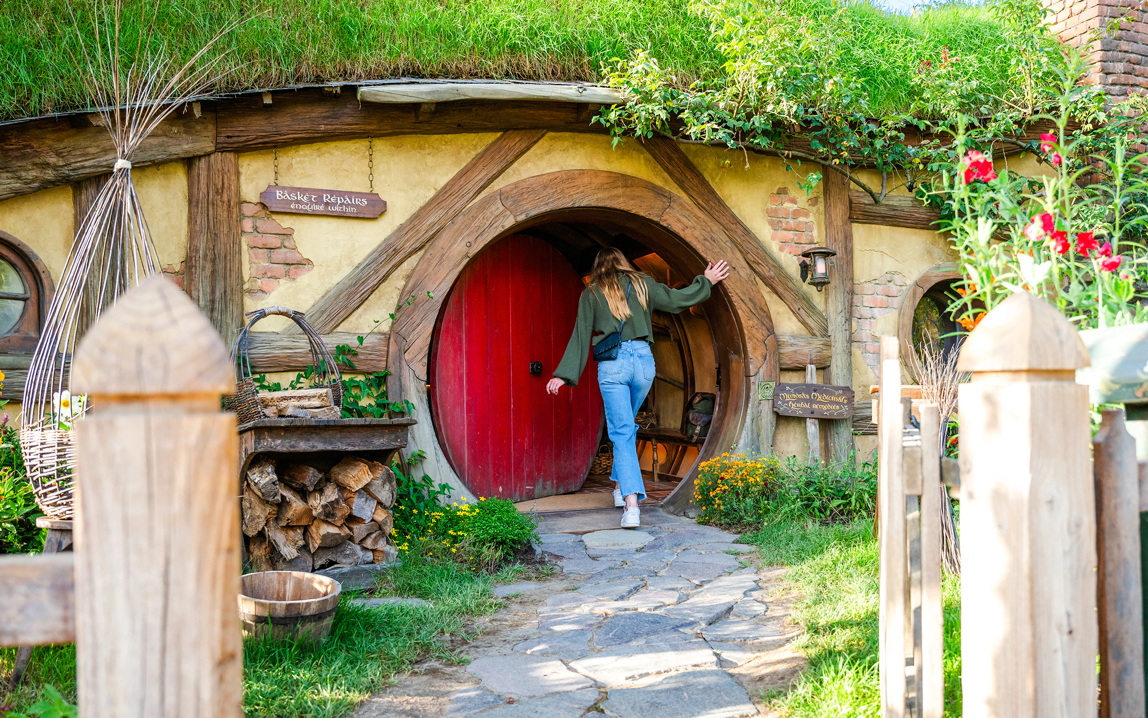 Visitors posing at Hobbiton Movie Set, New Zealand, with iconic hobbit house in background.