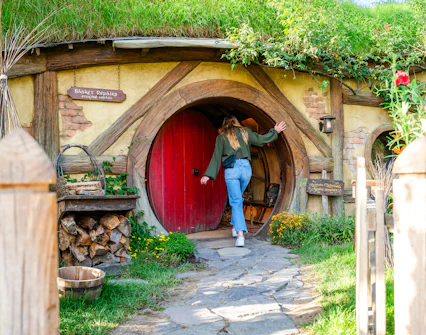 Woman entering round door of hobbit house, Hobbiton movie set tour.