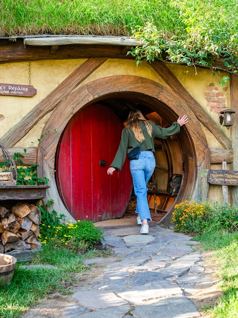 Woman entering round door of hobbit house, Hobbiton movie set tour.