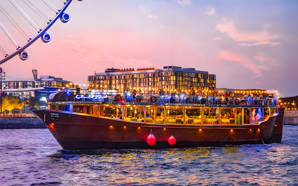 Luxury dhow cruise near Ain Dubai at sunset, with cityscape in the background.