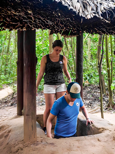 Visitors entering Cu Chi tunnel with guide in Vietnam forest.