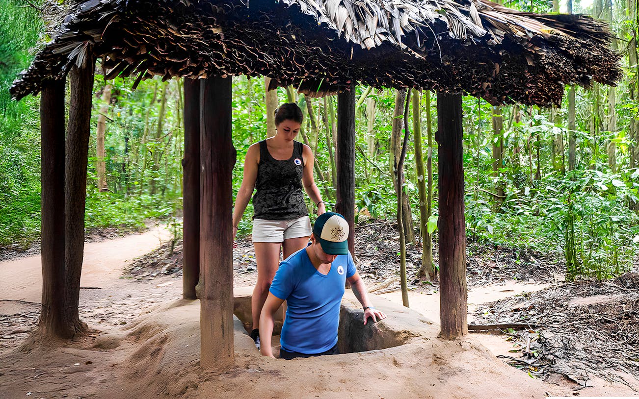 Visitors entering Cu Chi tunnel with guide in Vietnam forest.