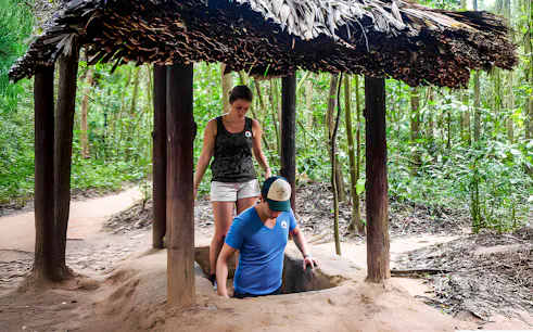 Visitors entering Cu Chi tunnel with guide in Vietnam forest.
