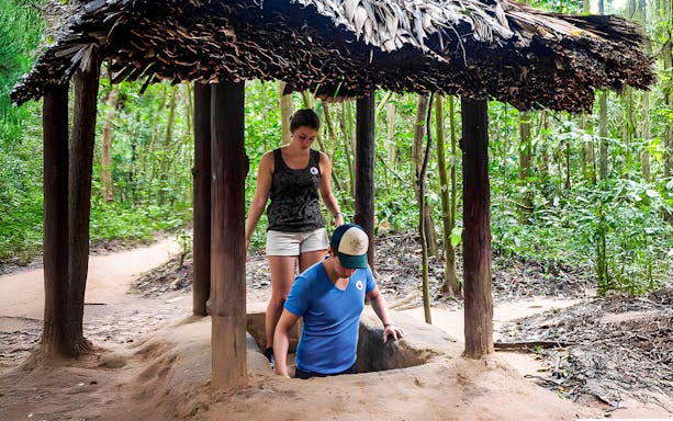 Visitors entering Cu Chi tunnel with guide in Vietnam forest.
