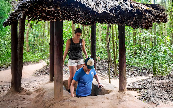 Visitors entering Cu Chi tunnel with guide in Vietnam forest.