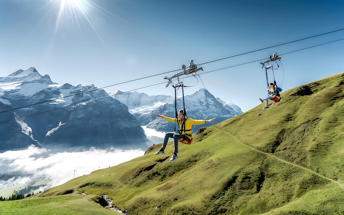 Person zip lining at Grindelwald First with Swiss Alps in the background.