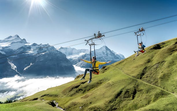 Person zip lining at Grindelwald First with Swiss Alps in the background.