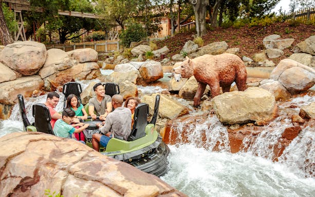 Rafting adventure on Calico River Rapids at Knott's Berry Farm with bear statue nearby.