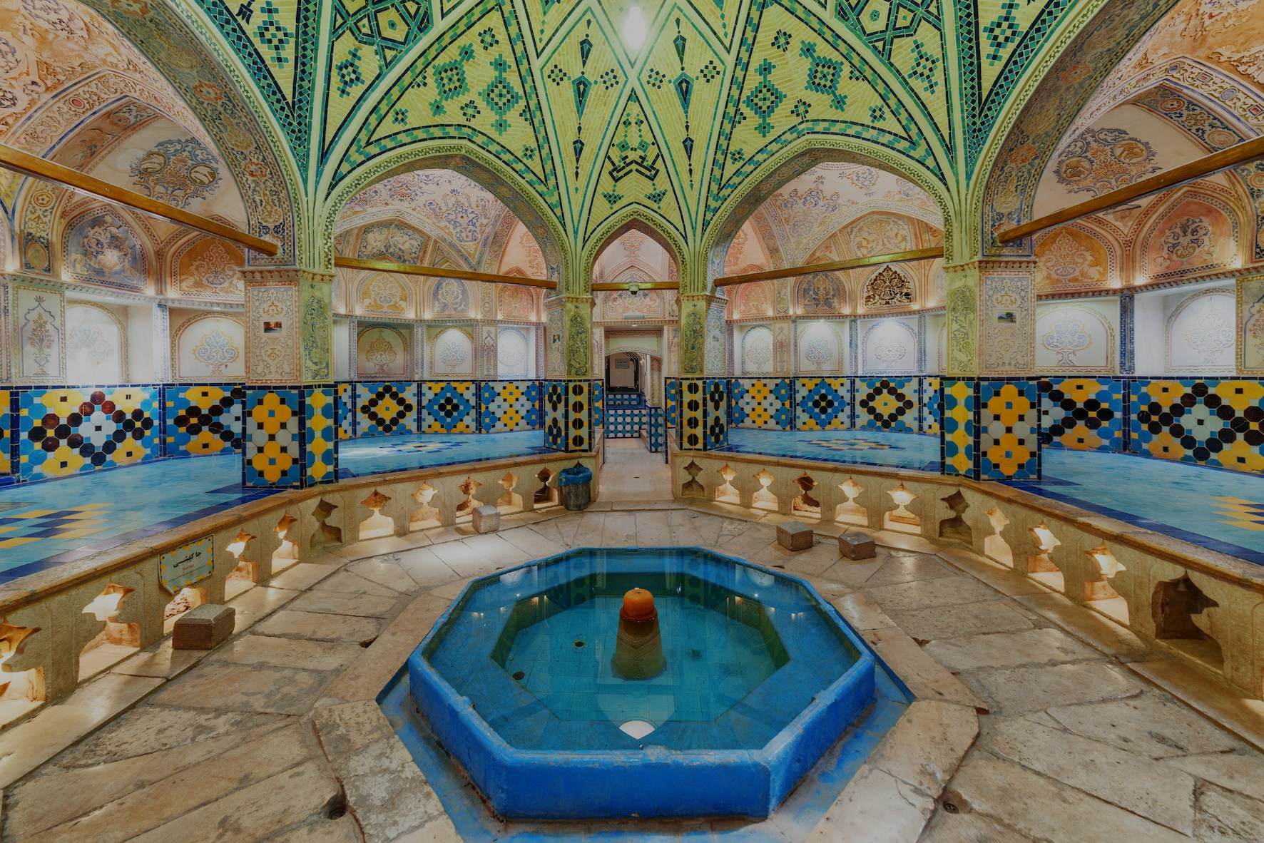 Turkish hammam interior with ornate tilework and central fountain.