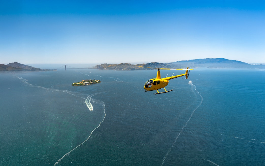 Helicopter flying near Alcatraz Island with Golden Gate Bridge in background.