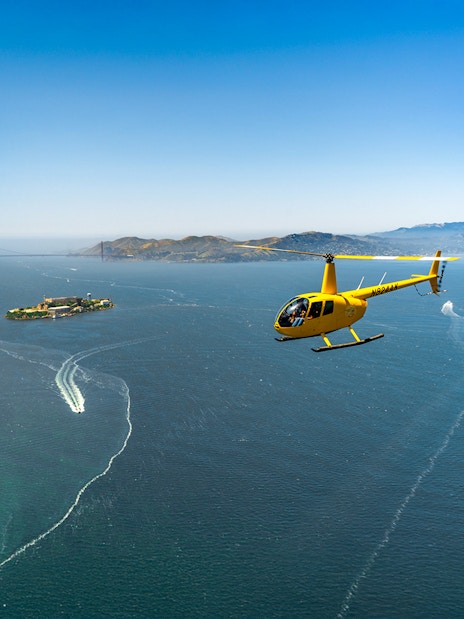 Helicopter flying near Alcatraz Island with Golden Gate Bridge in background.