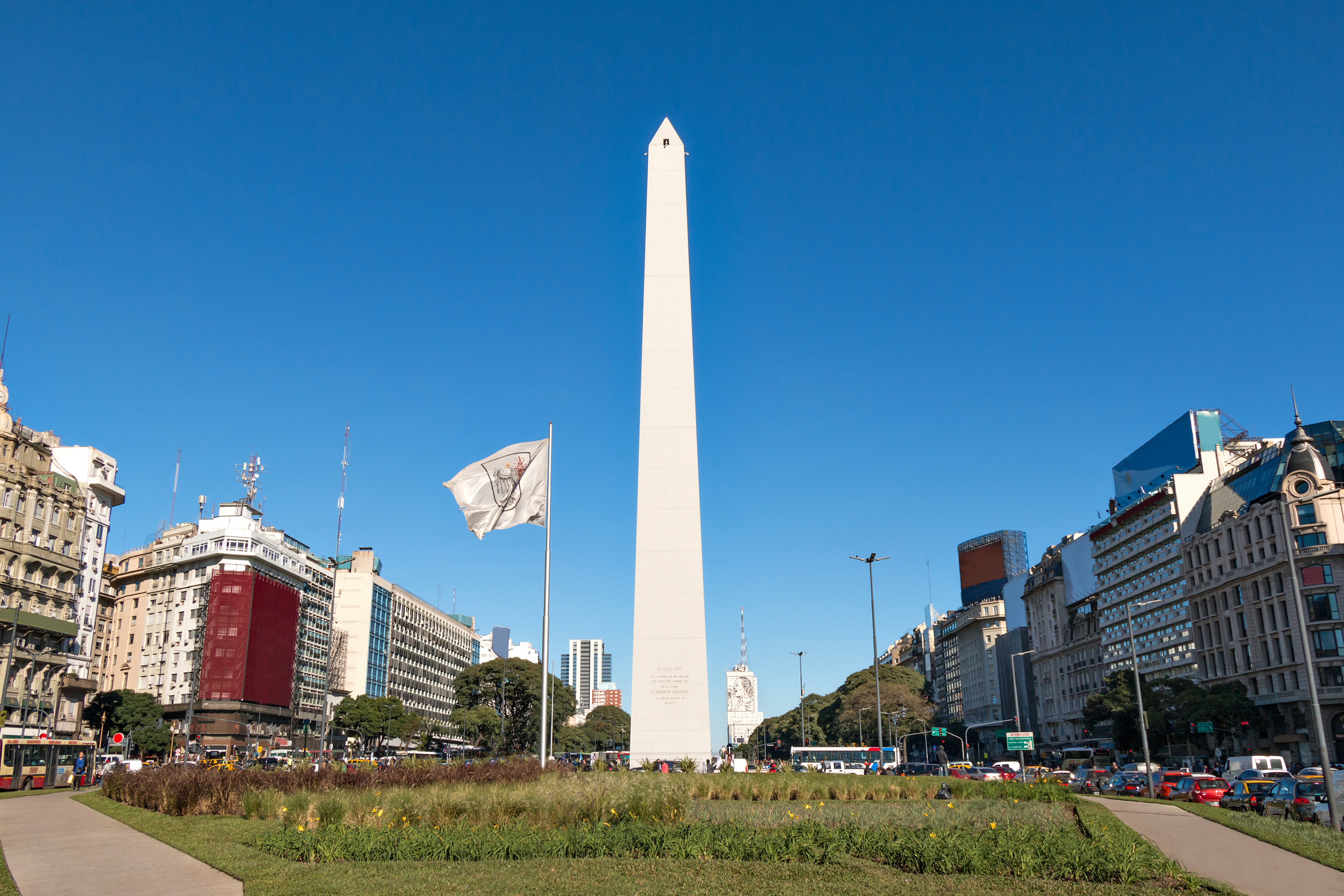Obelisk in Buenos Aires, Argentina, surrounded by city buildings and a flag.