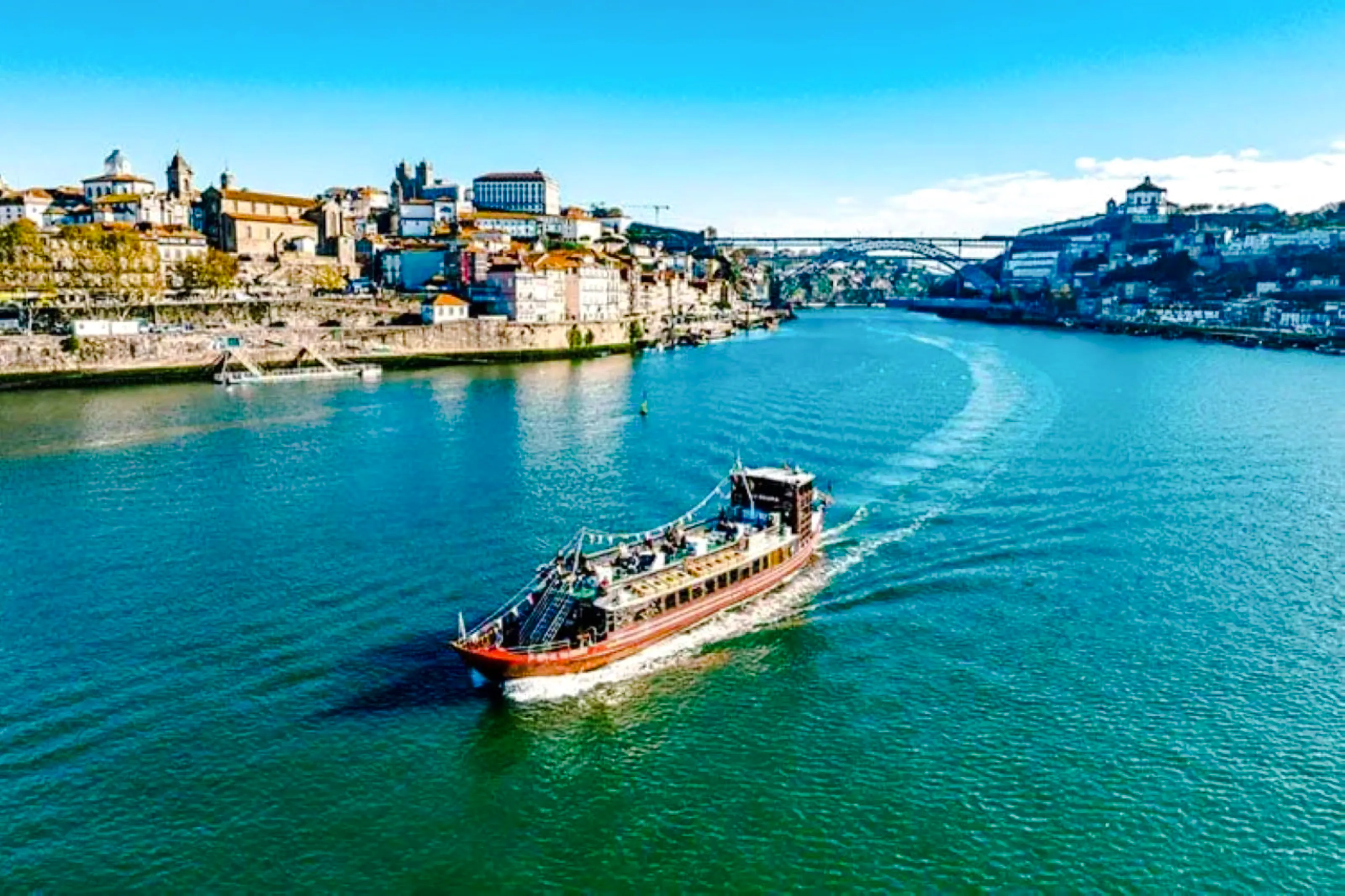 Cruise boat on Douro River with Porto cityscape and bridge in the background.