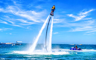 Person flyboarding over ocean in Tanjung Benoa, Bali with jet ski nearby.
