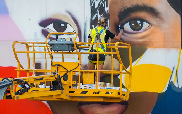 Artist painting a large mural on a lift during a 3.5-hour gourmet lunch or dinner and art tour.