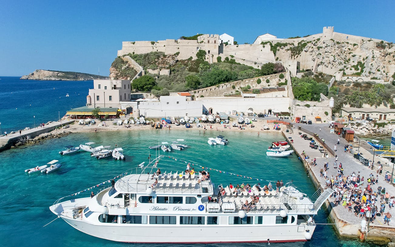 Ferry docked at Tremiti Islands with tourists boarding, Rodi Garganico in the background.