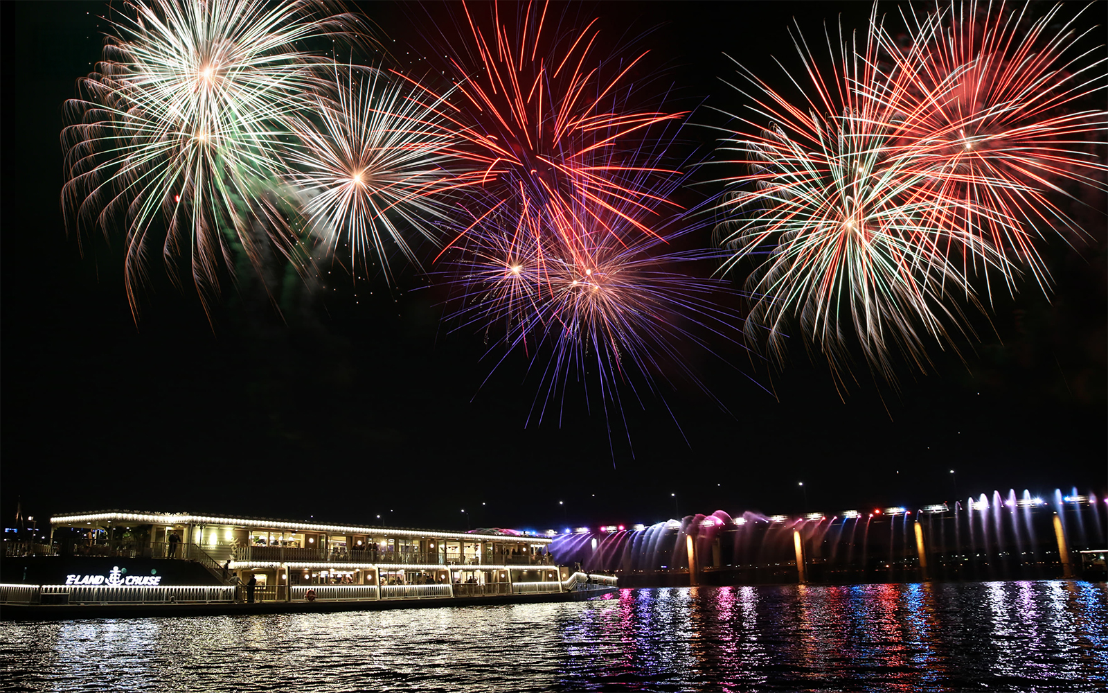 Fireworks display over a river cruise ship at night.