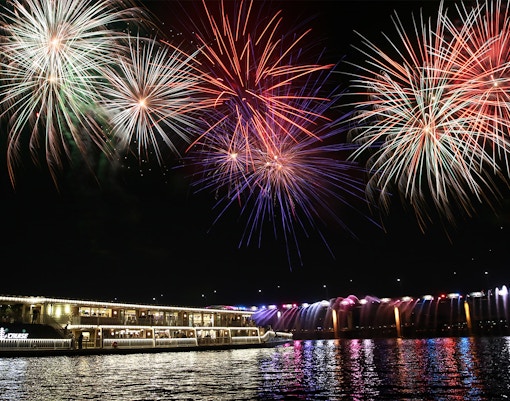 Fireworks display over a river cruise ship at night.