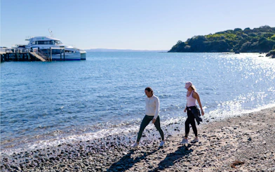 Visitors walking along the beach near ferry dock on Tiritiri Matangi Island, New Zealand.