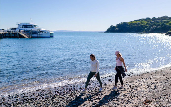 Visitors walking along the beach near ferry dock on Tiritiri Matangi Island, New Zealand.