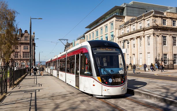 Edinburgh tram on city street, used for airport transfer.