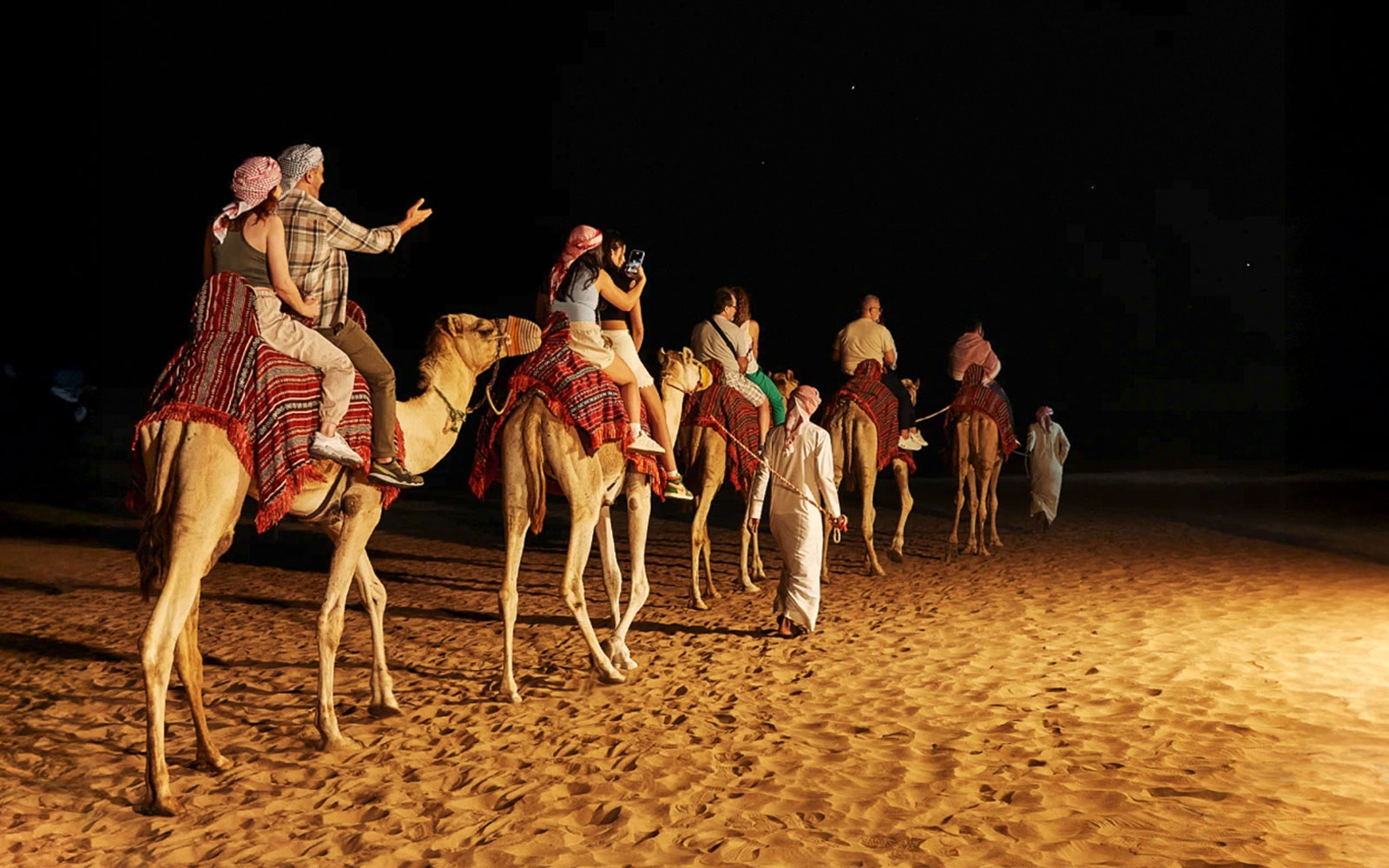 People sitting on a camel during a night safari in Dubai desert.