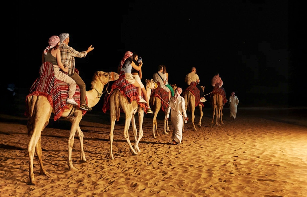 People sitting on a camel during a night safari in Dubai desert.