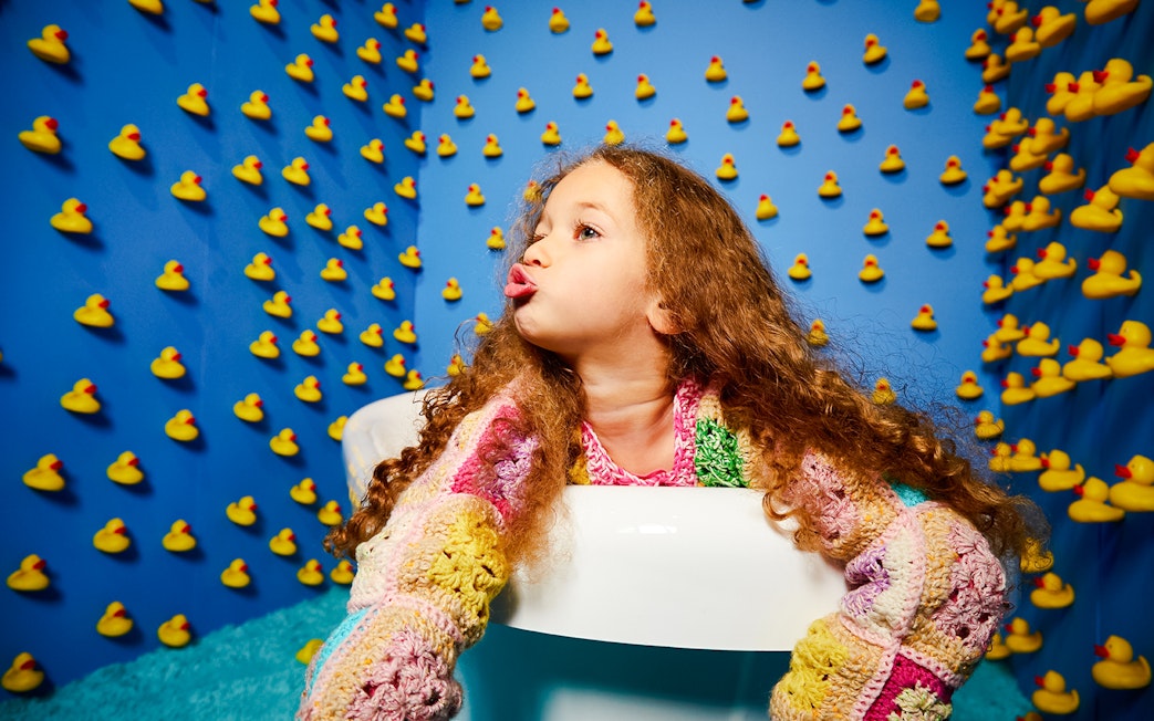 Child in a colorful sweater surrounded by rubber ducks at Bubble Planet, Seattle.