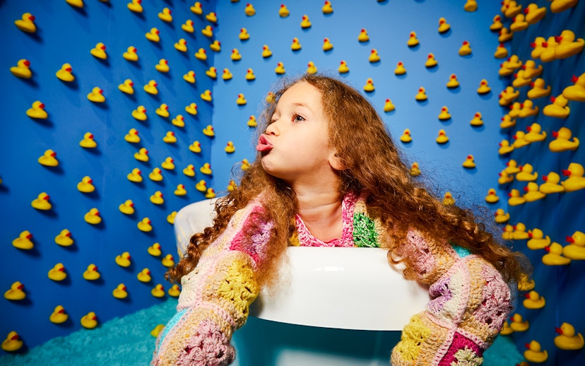 Child in a colorful sweater surrounded by rubber ducks at Bubble Planet, Seattle.