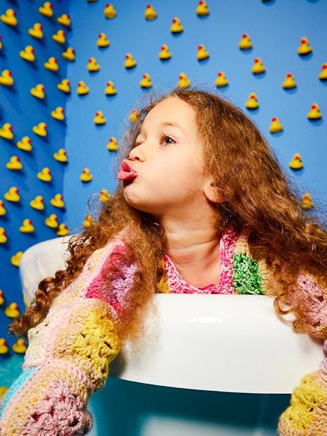 Child in a colorful sweater surrounded by rubber ducks at Bubble Planet, Seattle.
